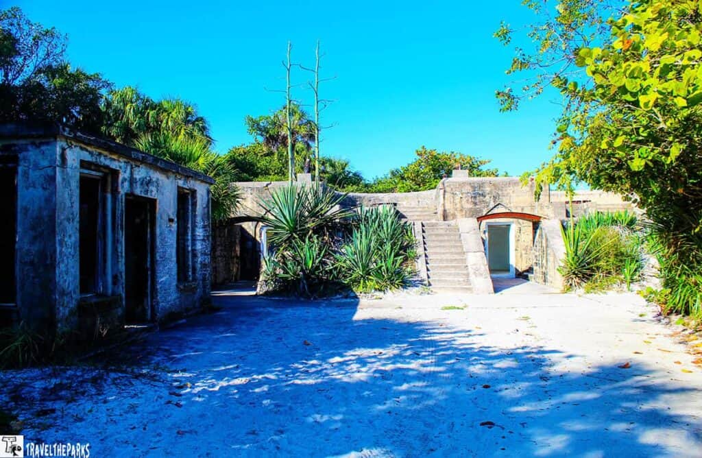 Ruins of Fort Dade on Egmont Key with stone structures and surrounding greenery under a bright blue sky.

