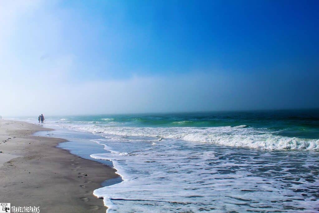 A tranquil beach scene on the Florida suncoast with soft sand, gentle waves, and two people walking along the shore.

