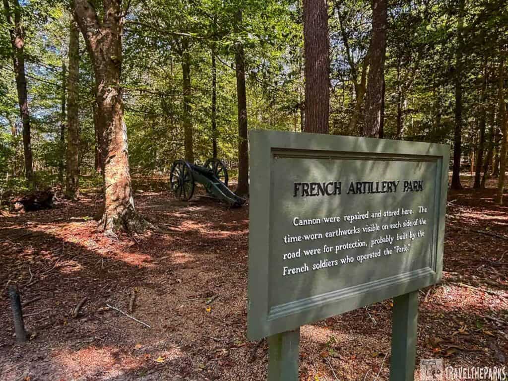A wooded area with a historical sign reading "French Artillery Park" and a cannon in the background.