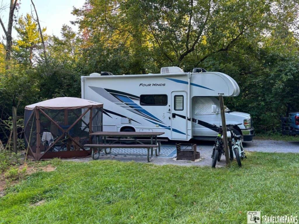 A motorhome and camping setup at Gambrill State Park with a screened tent, picnic table, fire pit, and bicycles.