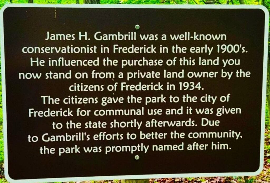 Informational sign about James H. Gambrill and the park's history. Transcribed Text: James H. Gambrill was a well-known conservationist in Frederick in the early 1900's. He influenced the purchase of this land you now stand on from a private land owner by the citizens of Frederick in 1934. The citizens gave the park to the city of Frederick for communal use and it was given to the state shortly afterwards. Due to Gambrill's efforts to better the community, the park was promptly named after him.