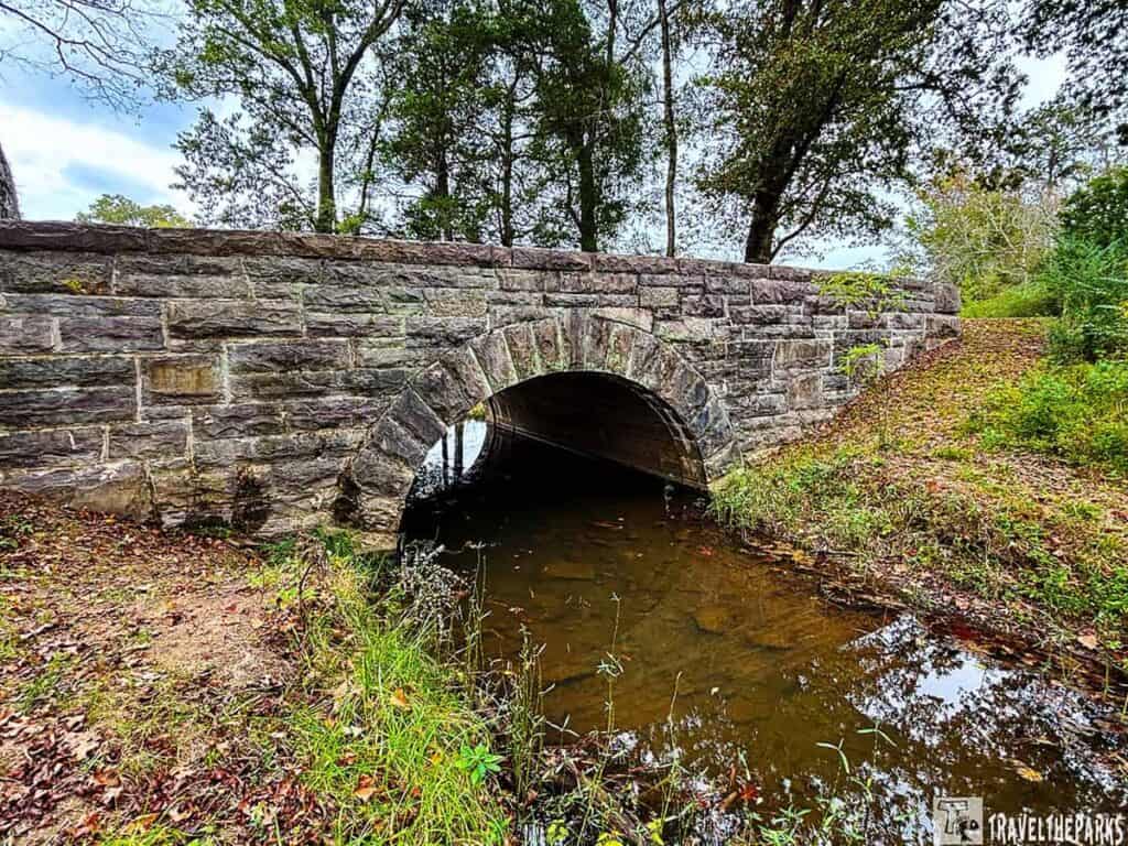 Passageway under LaFayette Road near the Chickamauga Battlefield Visitor Center. Stone bridge over a creek with trees and greenery.

