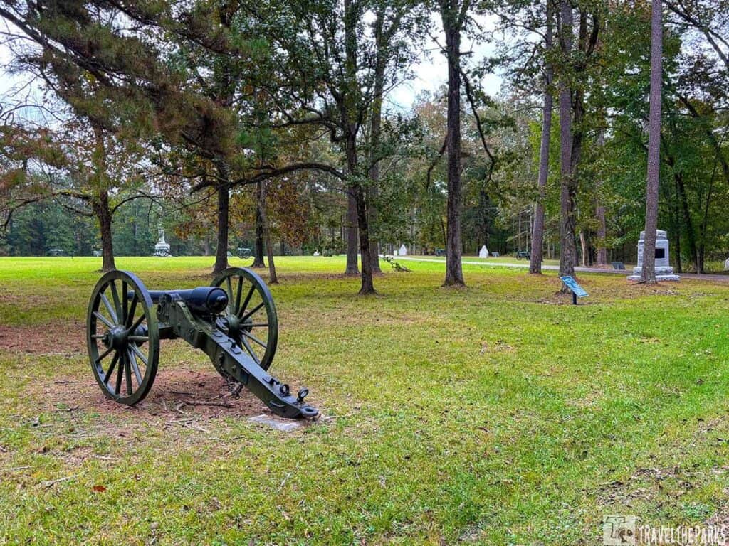 A historical cannon on grassy field with trees and monuments in Chickamauga and Chattanooga National Military Park.