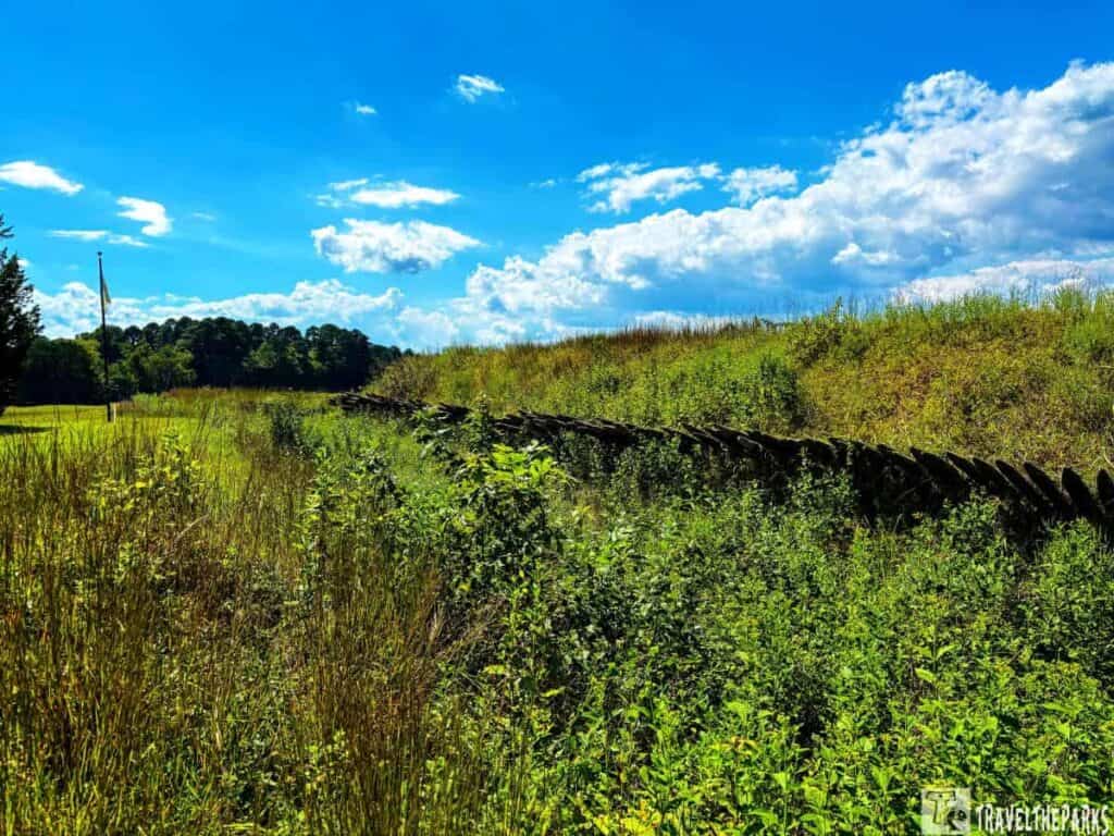 Scenic view of Redoubt 9 at Yorktown National Battlefield with tall grasses, a wooden fence, and a flagpole in the distance.