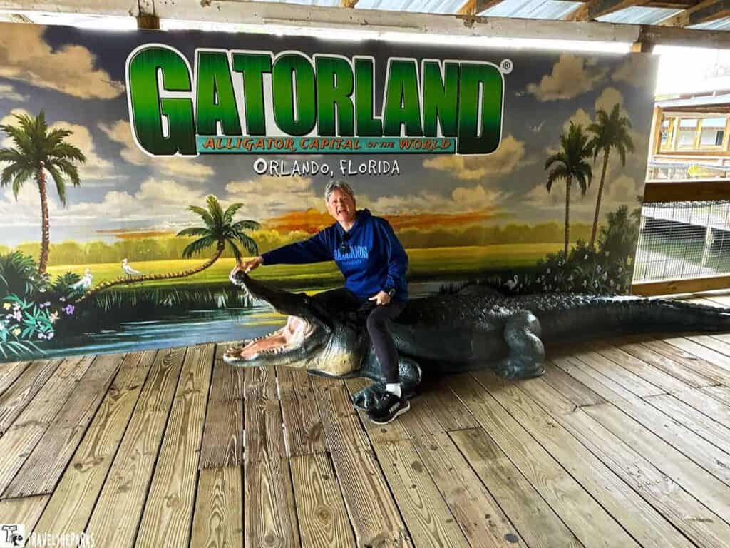 Person sitting on a large alligator statue in front of a mural at Gatorland Orlando.

