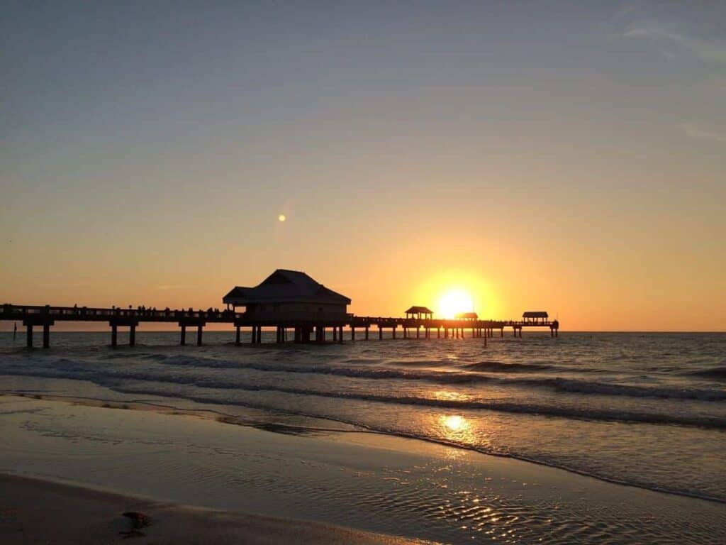 Sunset view of Clearwater Beach Pier 60 with silhouettes of people and a calm ocean.

