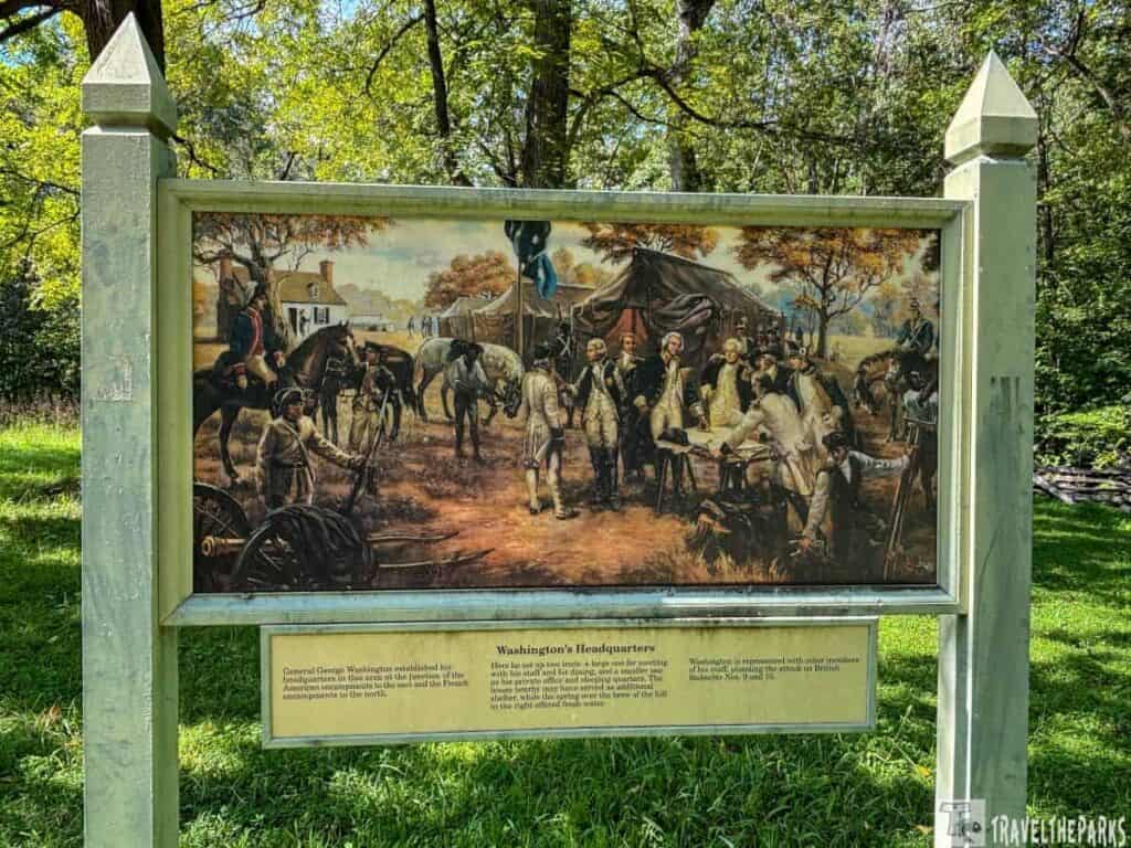 Outdoor sign with a historical painting showing Revolutionary War soldiers and a tent.