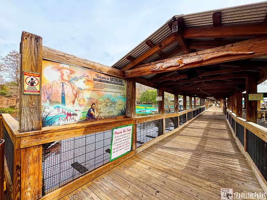 Wooden boardwalk at Gatorland Orlando with a welcome sign featuring alligator artwork and safety notices.

