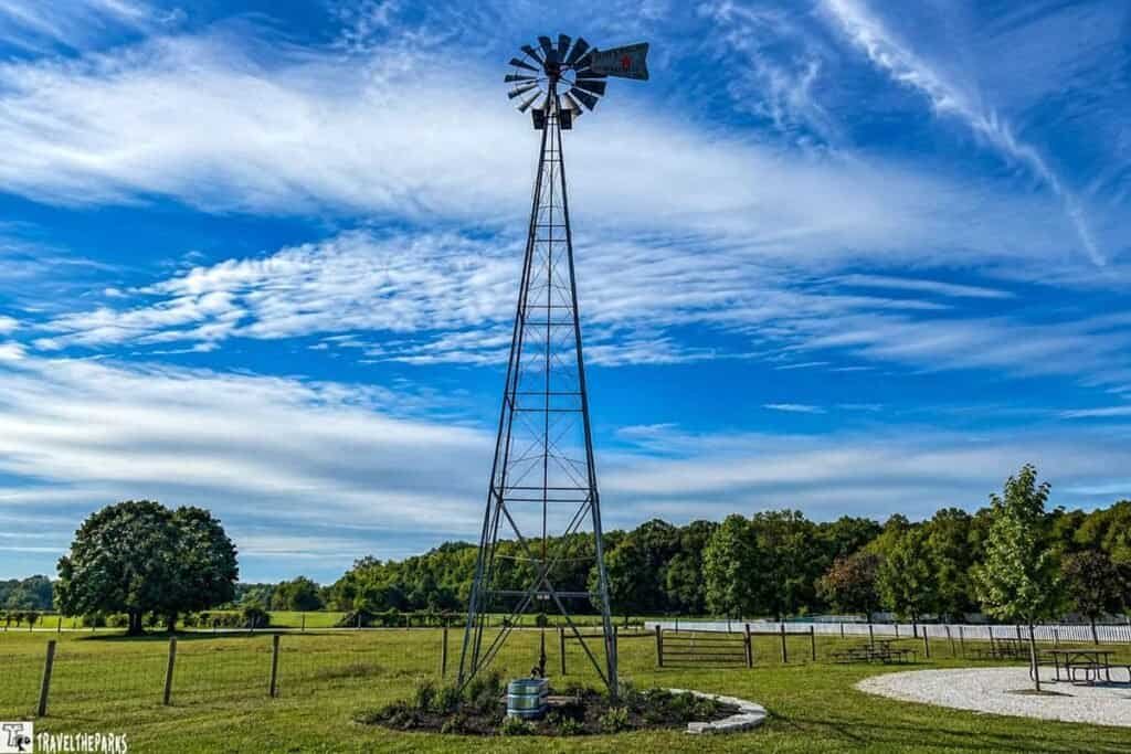 Tall windmill in a grassy field with blue sky and scattered clouds.