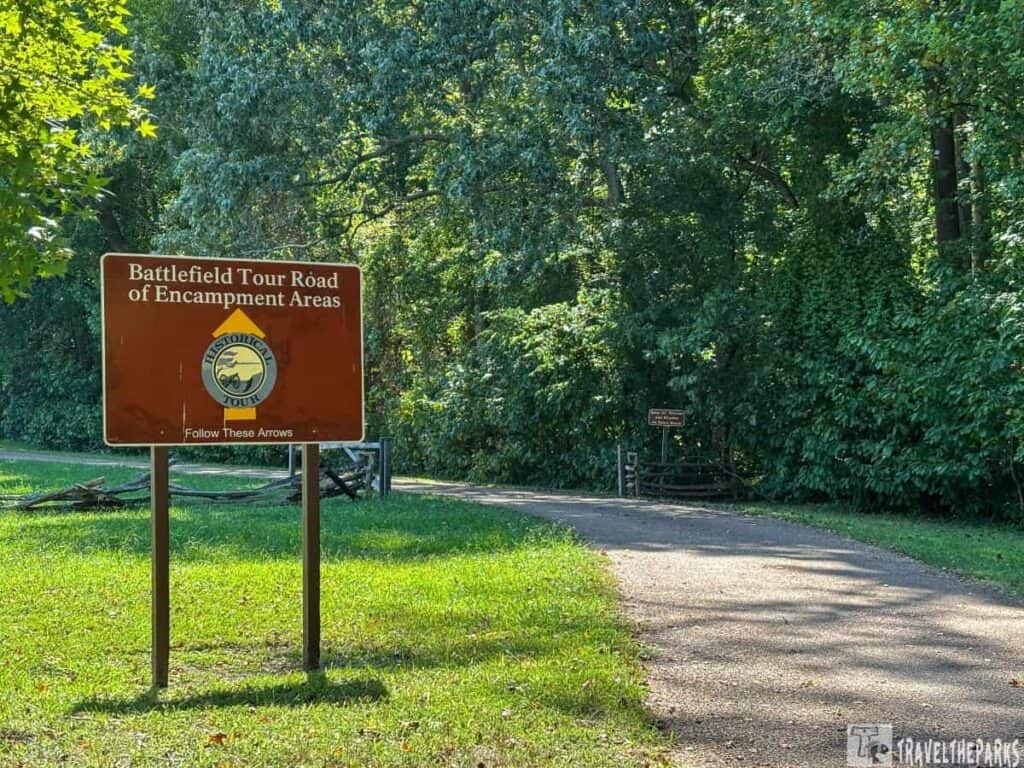 A brown sign for "Battlefield Tour Road of Encampment Areas" by a forested pathway.
