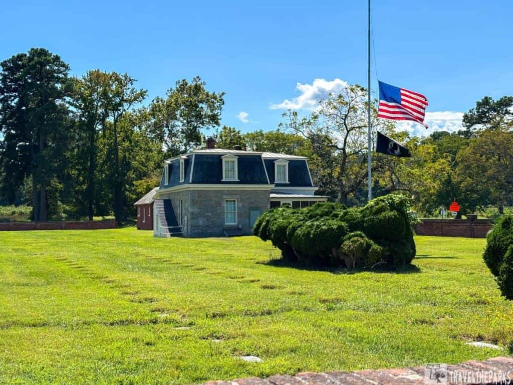 Historic stone house at Yorktown National Cemetery with flags at half-mast and lush greenery.