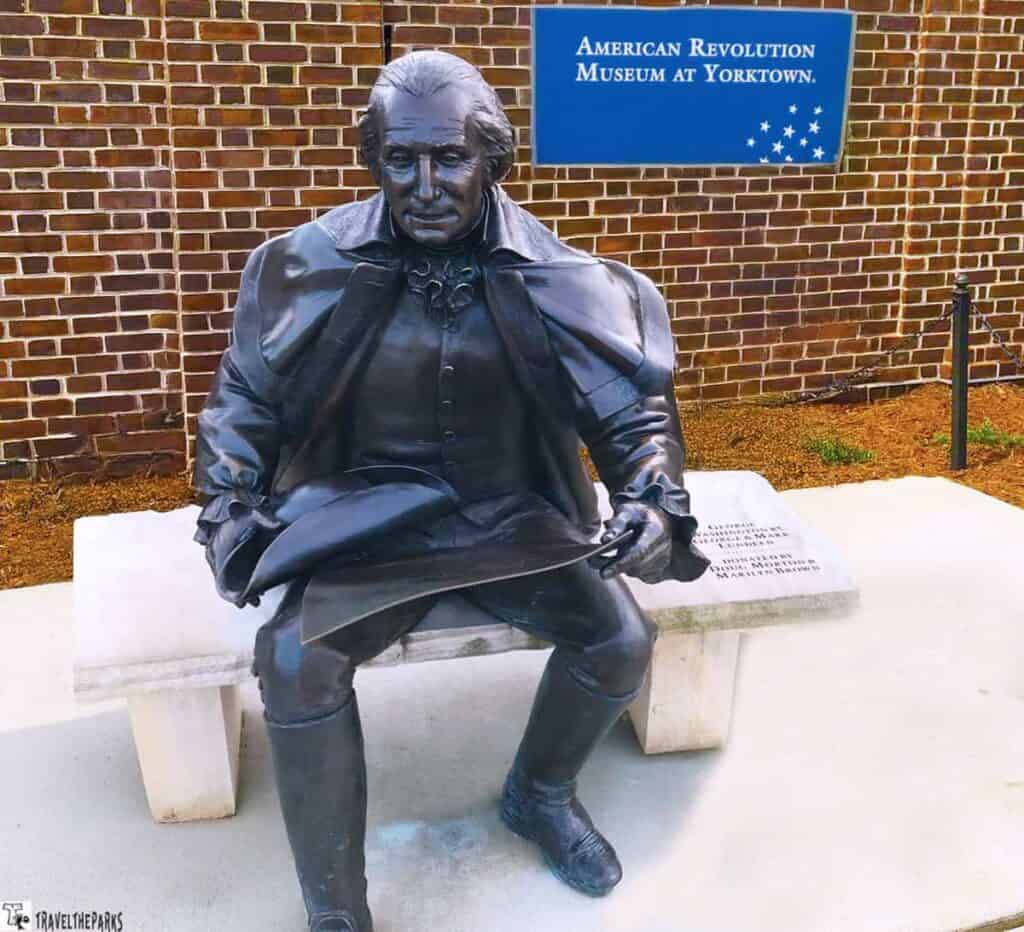 Bronze statue of a seated historical figure with a tricorn hat in front of a sign reading "American Revolution Museum at Yorktown."

