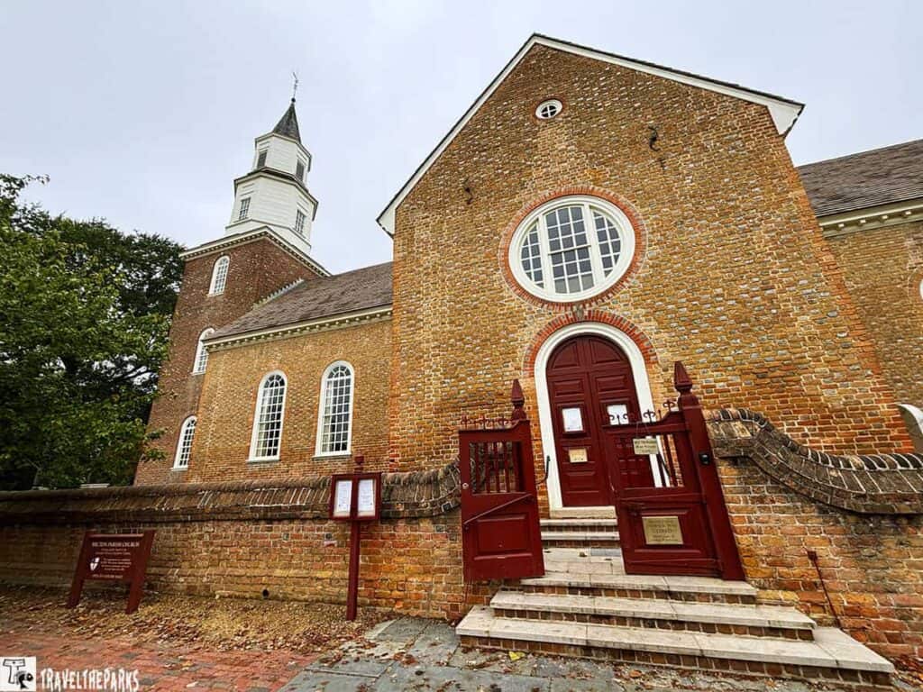 Historic red brick church with arched windows and a white bell tower, featuring a red entrance door and an oval window above.