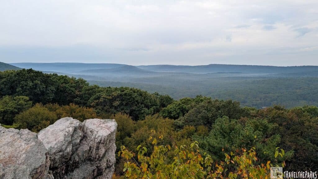 Scenic view of Shenandoah River State Park with rock formations, dense green foliage, distant misty hills, and an overcast sky.
