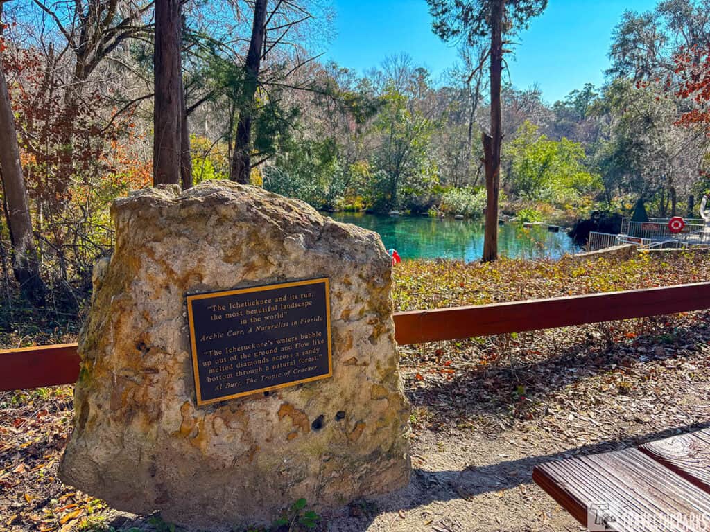 A rock with a plaque in front of a spring surrounded by trees at Ichetucknee Springs State Park.