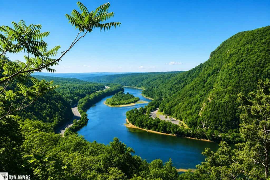 View of a winding river through verdant hills, framed by tree branches under a clear blue sky.