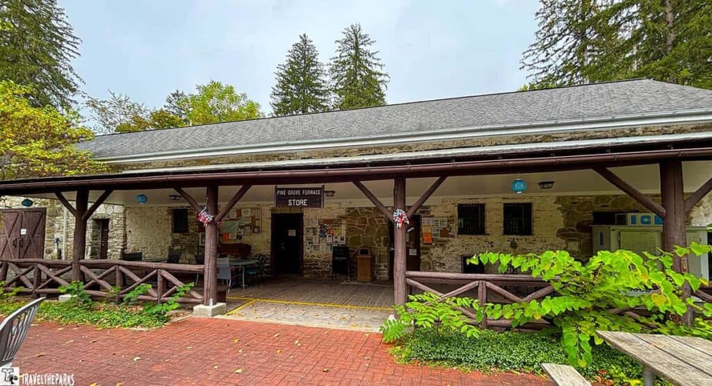 A rustic, wood‑framed general store with a covered porch and railing, tucked into the forested grounds of Pine Grove Furnace State Park.