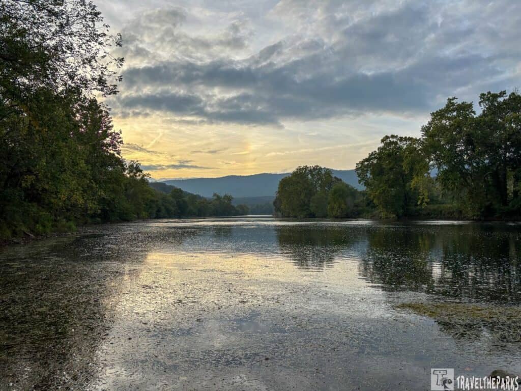 A calm river at sunrise or sunset with trees and mountain silhouettes at Shenandoah River State Park.