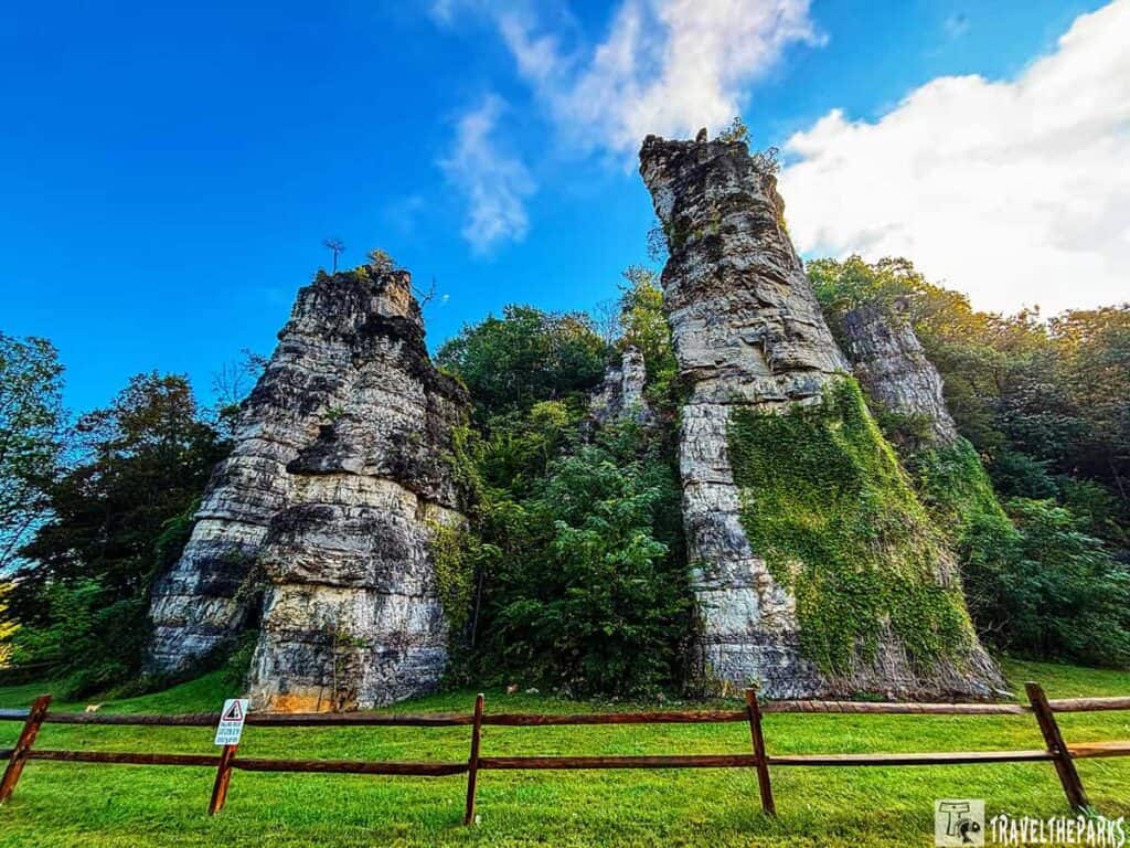 Tall limestone rock formations at Natural Chimneys Park with a bright blue sky and green foliage.