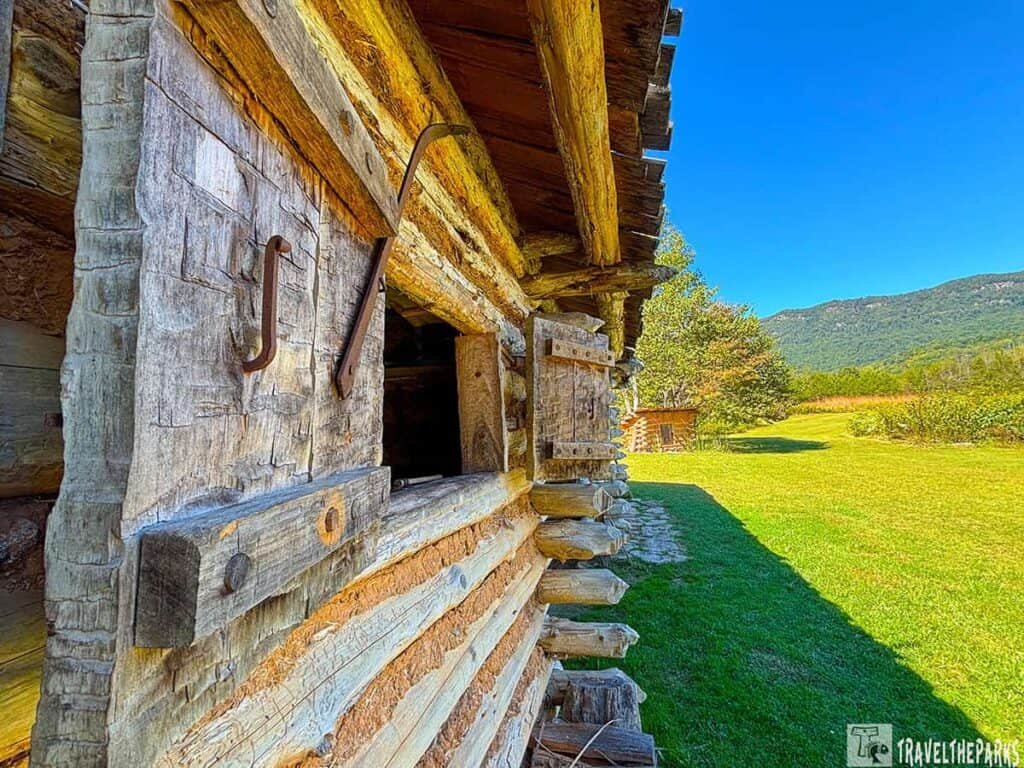 Close-up of a rustic log cabin with a grassy field and hills in the background.