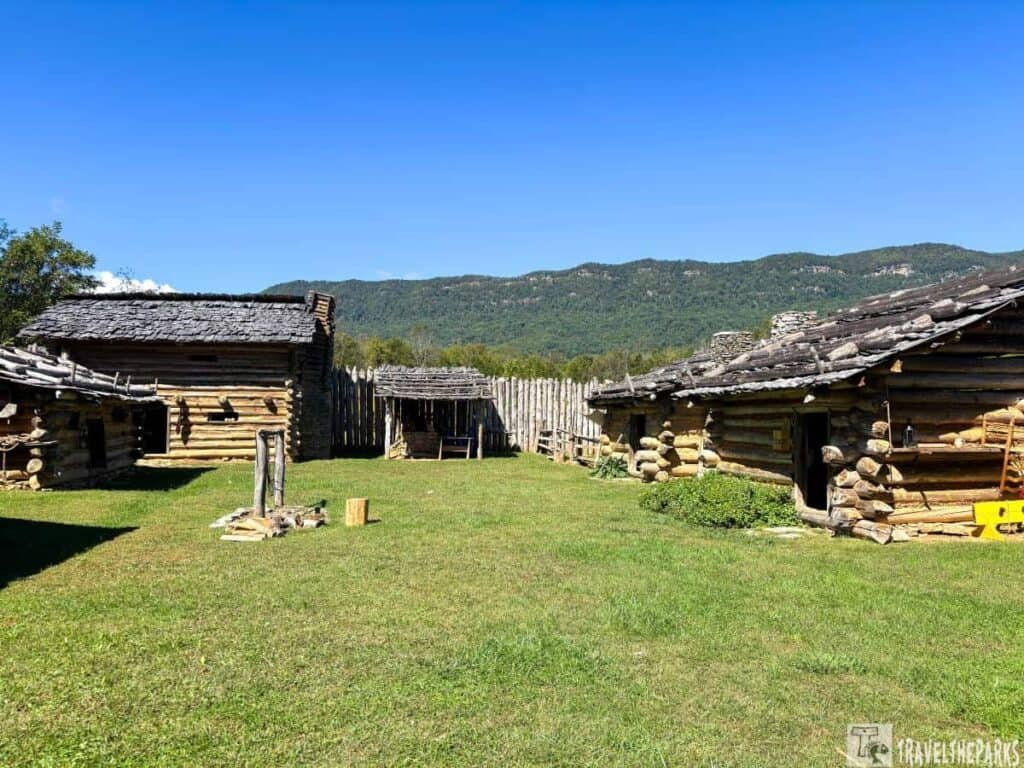 Log cabins and a palisade fence at Martin Station in Wilderness Road State Park with hills in the background.