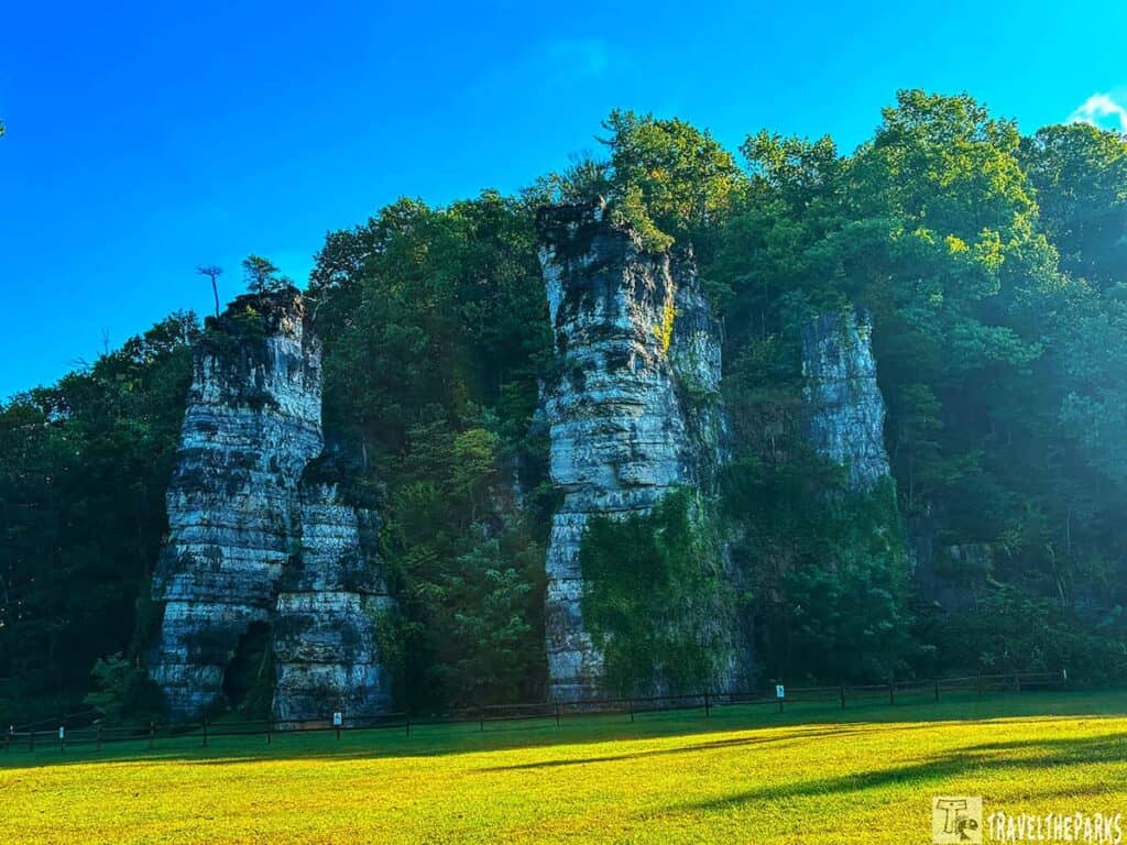 Tall limestone rock formations at Natural Chimneys Park with a bright blue sky and green foliage.