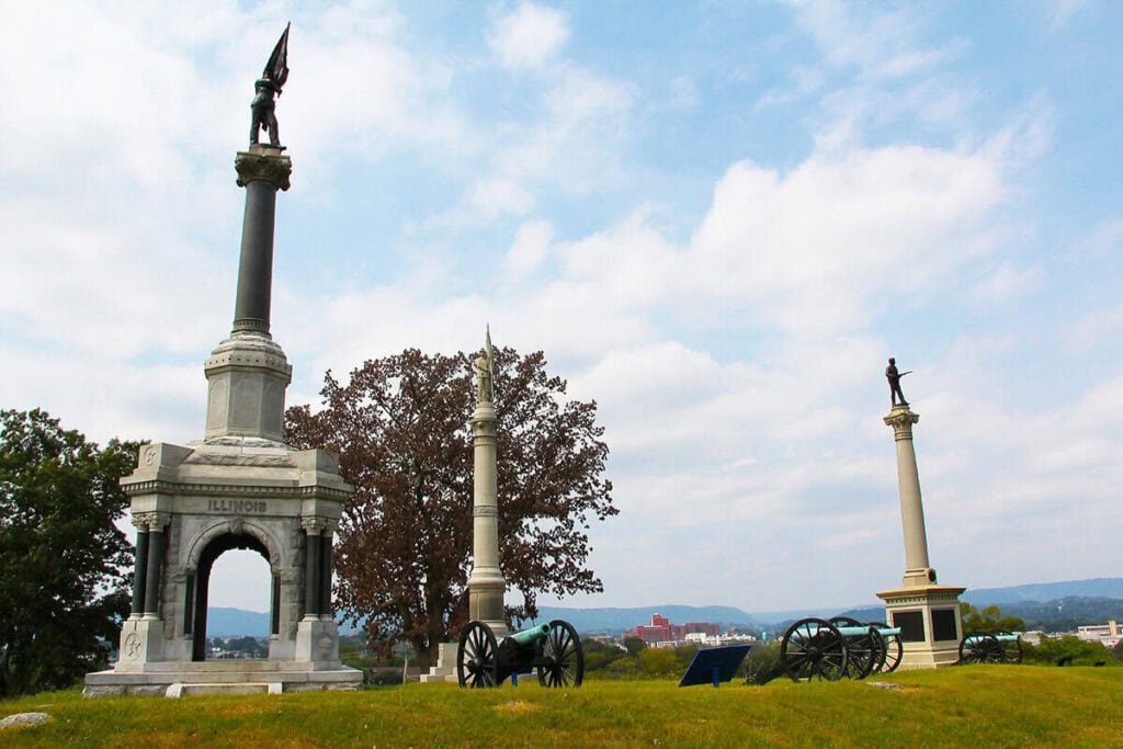 Historical monuments and cannons at Orchard Knob on a grassy hill with a cityscape in the background.
