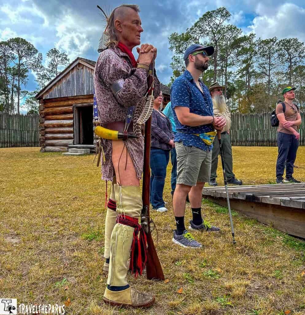 A group of people at a historic reenactment in front of a wooden fort.