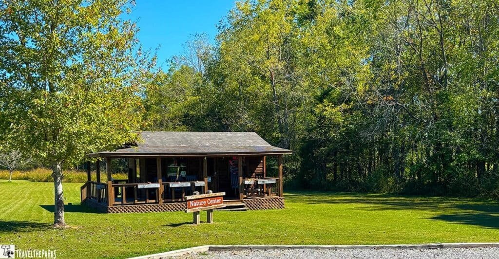 Rustic cabin labeled "Nature Center" surrounded by trees with a grassy lawn.