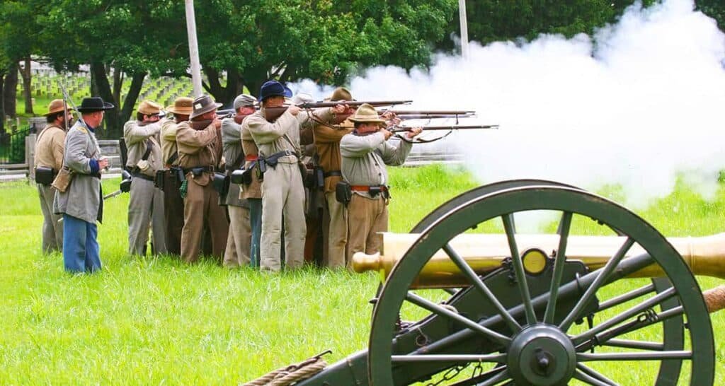 A group of Civil War reenactors firing rifles behind a large cannon at Stones River National Battlefield.

