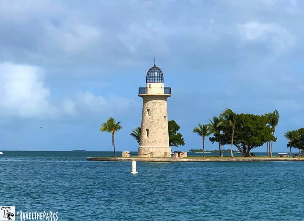 Stone Boca Chita lighthouse with a glass dome on an island with palm trees and surrounded by water.

