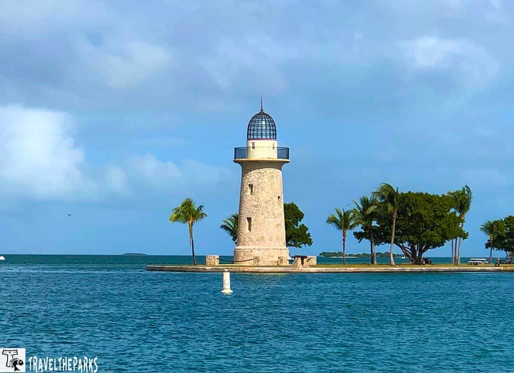 Stone Boca Chita lighthouse with a glass dome on an island with palm trees and surrounded by water.