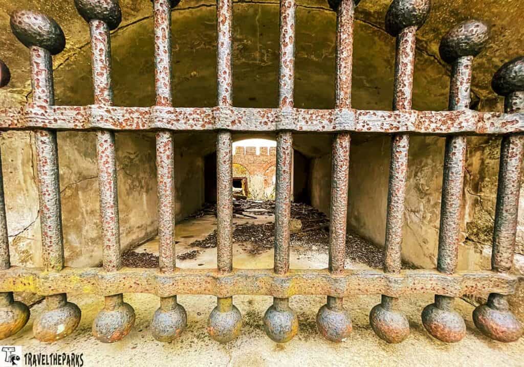 Dungeness Mansion View: Rusty iron gate in front of a stone tunnel, with a distant view of a brick archway.


