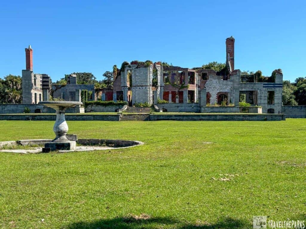 Dungeness Ruins on Cumberland Island with crumbling stone and brick walls, chimneys, and a manicured lawn in the foreground.