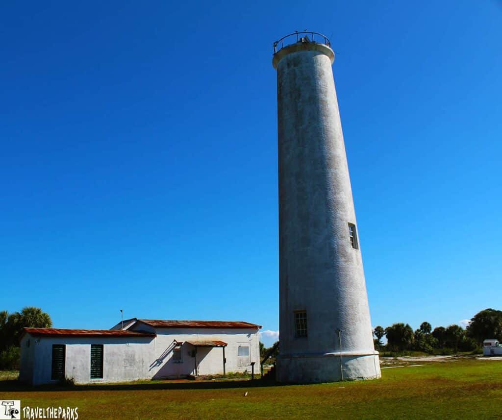 Egmont Key Lighthouse a tall, cylindrical white lighthouse next to a small, single-story building.