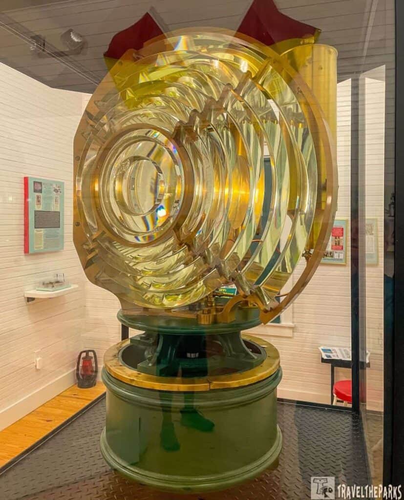 A large Fresnel lens on a green base in a museum display case.

