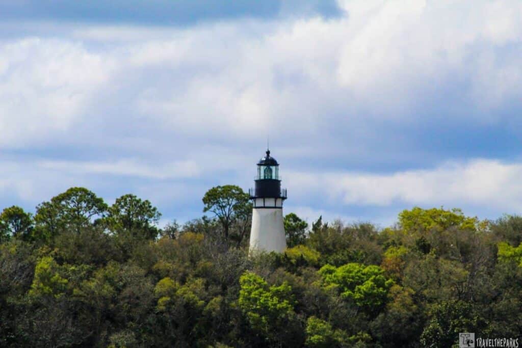 Amelia Island Lighthouse emerging from lush foliage under a cloudy sky.

