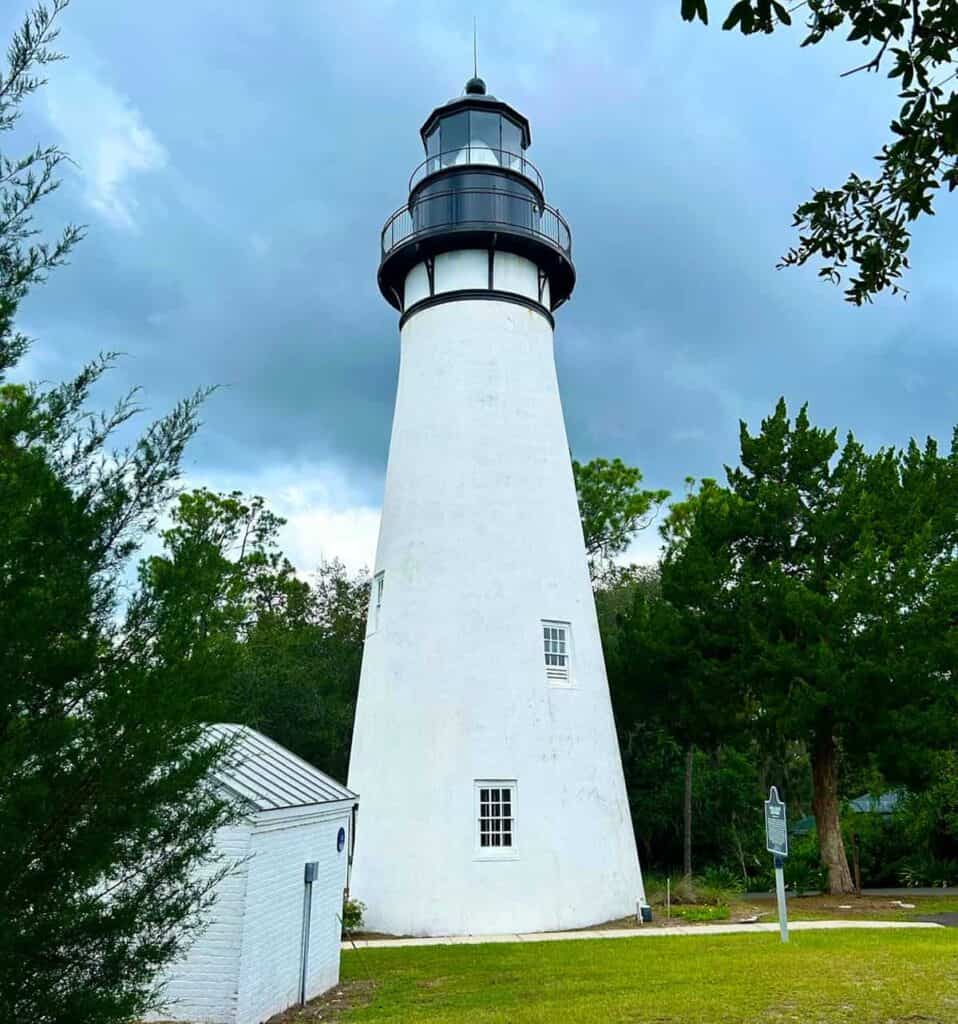 Amelia Island Lighthouse with surrounding greenery and cloudy sky.

