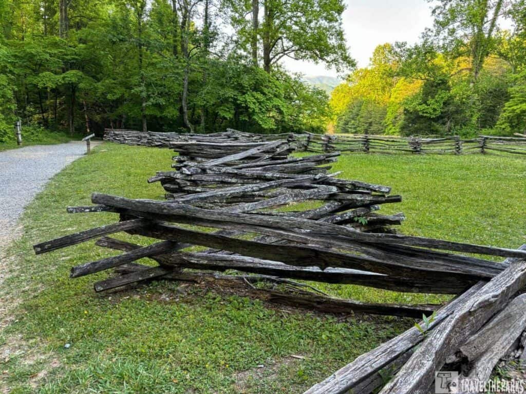 Cades Cove travel guide: A zigzag split-rail fence in a grassy field at Cades Cove, with trees and a gravel path nearby.