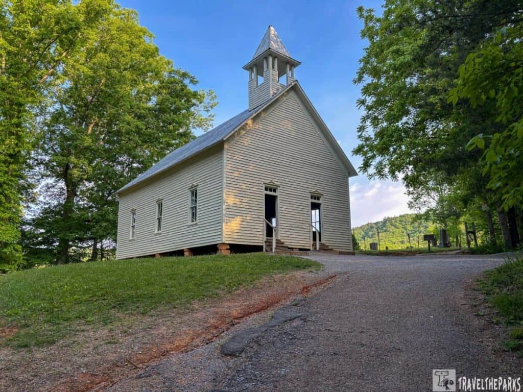 A white wooden Methodist church with a steeple, located in a grassy area of Cades Cove.

