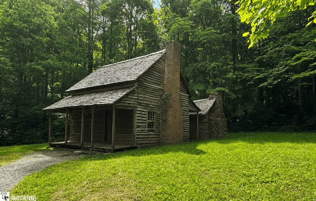 Henry Whitehead Place: Log cabin in a wooded area with a grassy lawn and gravel path.