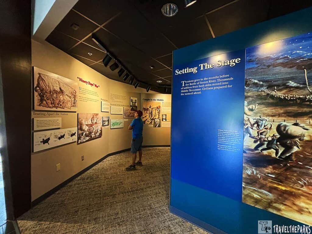 Interior of a museum exhibit on the Battle of Stones River, featuring historical panels and a visitor reading the information.

Transcribed Text:

“Ninety Days’ War”
“Tearing Apart the Nation”
“Caught in the Middle”
Setting The Stage
Tensions grew in the months before the Battle of Stones River. Thousands of soldiers from both sides moved into Middle Tennessee. Civilians prepared for the turmoil ahead.