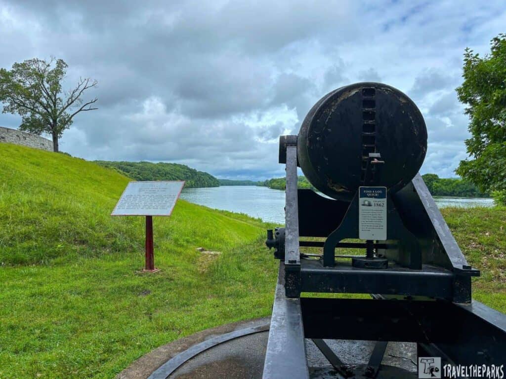 View of a black cannon at Fort Donelson, pointing towards a river, with grassy slopes and cloudy skies in the background.