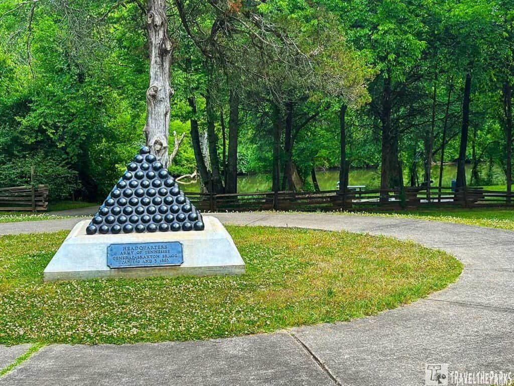 Pyramid-shaped memorial of cannonballs dedicated to General Braxton Bragg, surrounded by greenery and a pathway.

