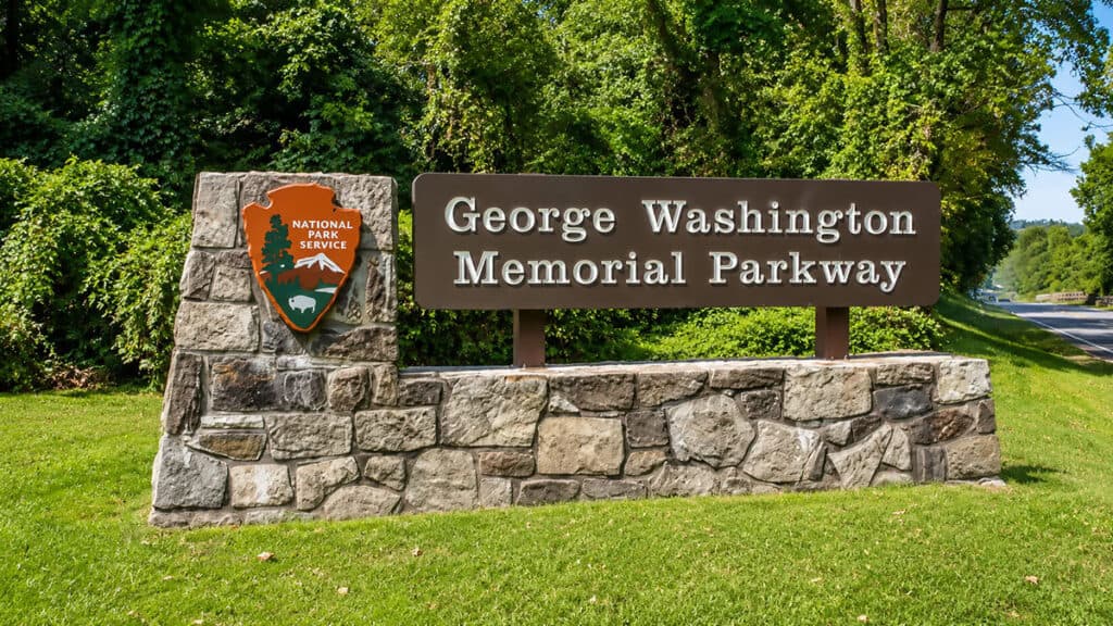 Virginia Scenic Byways: Stone sign for George Washington Memorial Parkway with National Park Service emblem, surrounded by greenery.