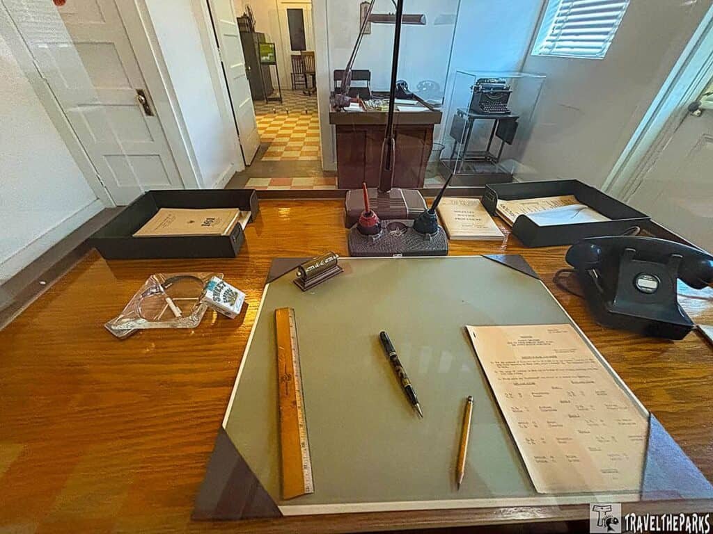 A historical desk setup with a glass writing surface, a rotary phone, inkwells, a yellow pencil, and a black pen, showcasing items associated with the Tuskegee Airmen.


