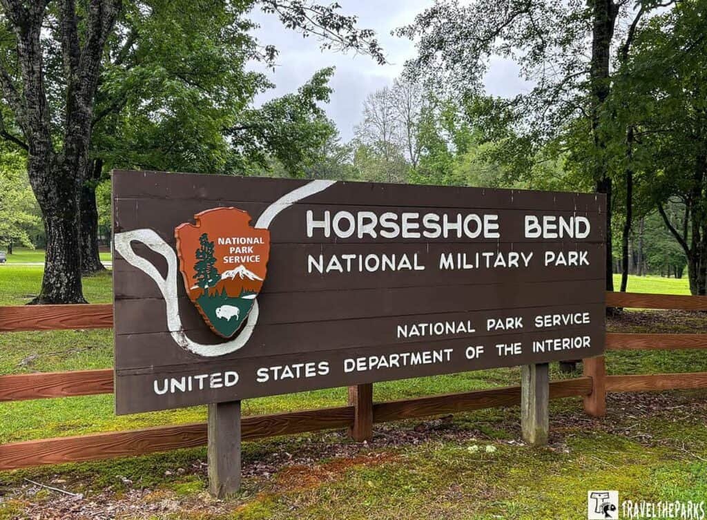 Wooden sign for Horseshoe Bend National Military Park displaying a colorful National Park Service emblem; text includes "Horseshoe Bend," "NATIONAL MILITARY PARK," "NATIONAL PARK SERVICE," and "UNITED STATES DEPARTMENT OF THE INTERIOR."