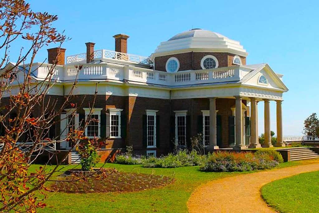 Exterior view of Monticello, showcasing its brick facade, white dome, columns, and the surrounding green landscape with a gravel path.
