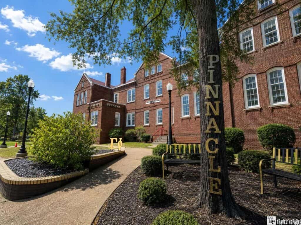 Old Administration Building at Tuskegee Institute featuring a landscaped pathway, a large tree with "PINNACLE" carved into its trunk, and benches in front of the building.

