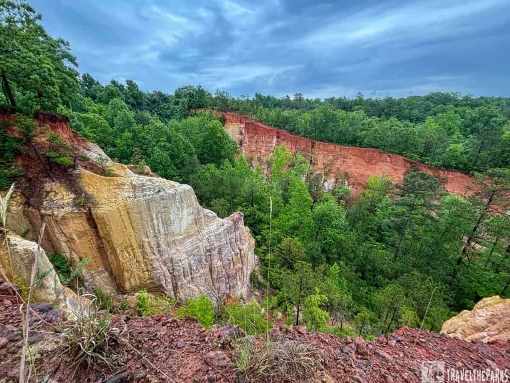 View of Providence Canyon with multicolored cliffs and lush green forest under a cloudy sky.